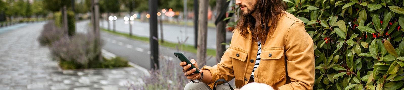 Man looking at hone while sitting on bench outdoors.