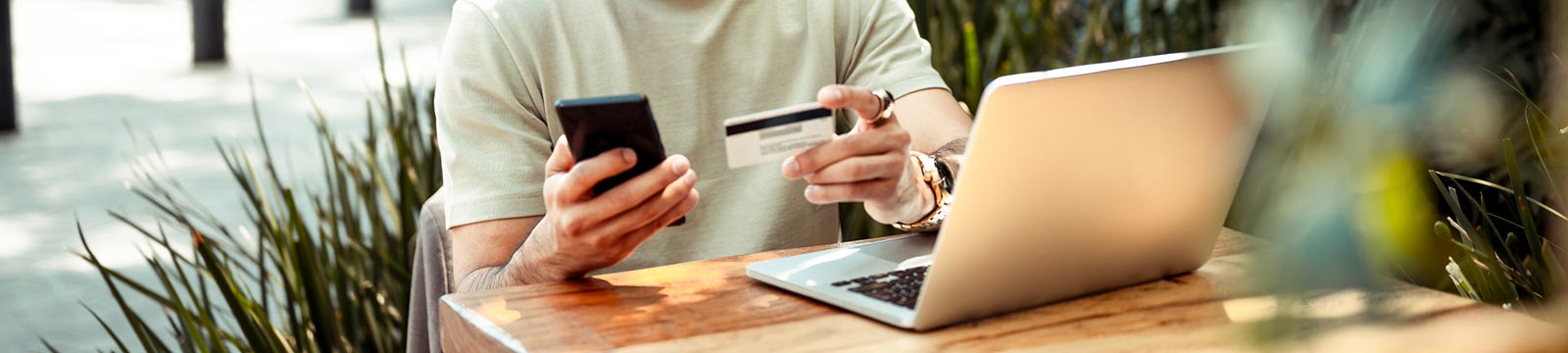 Man holding card and phone sitting in front of laptop.