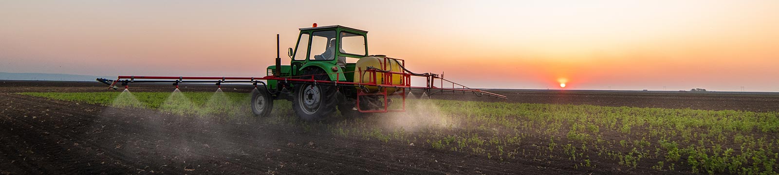 Tractor spraying crops at sunset.